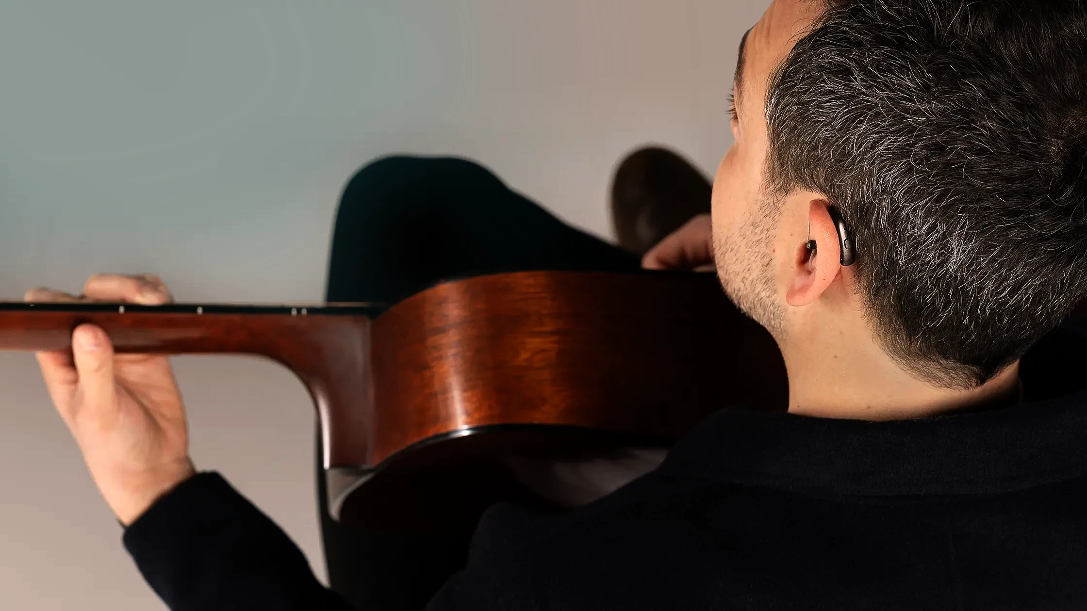 Ein Mann mit einem Hörsystem im Ohr spielt eine akustische Gitarre.